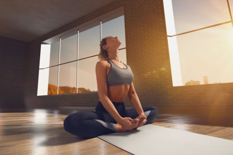Een vrouw in sportkleding doet yoga op een mat in een zonovergoten kamer – het beste moment om yoga te doen ter ontspanning en om tot rust te komen.