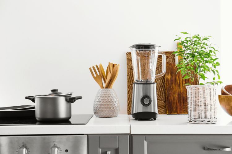 Een modern aanrecht met een pan op het fornuis, snijplanken en een van de beste smoothieblenders, naast keukengerei en een potplant.