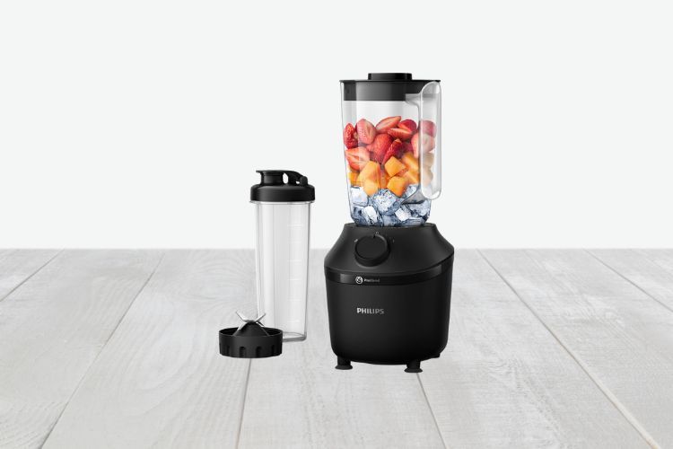 Een zwarte Philips 3000 series HR2041/41 Blender gevuld met gehakte vruchten en ijs staat op een licht houten oppervlak. Ernaast staat een heldere, cilindrische meeneemfles met een zwarte dop; het afneembare mesbevestiging is naast de fles geplaatst.