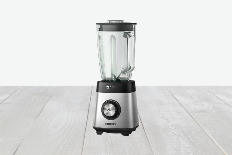 Afbeelding van een Philips Series 5000 Blender op een houten oppervlak. De blender heeft een transparante glazen kan met een handvat, een zwart deksel en een roestvrijstalen basis met een zwarte bedieningsknop aan de voorkant. De achtergrond is effen en lichtgekleurd.