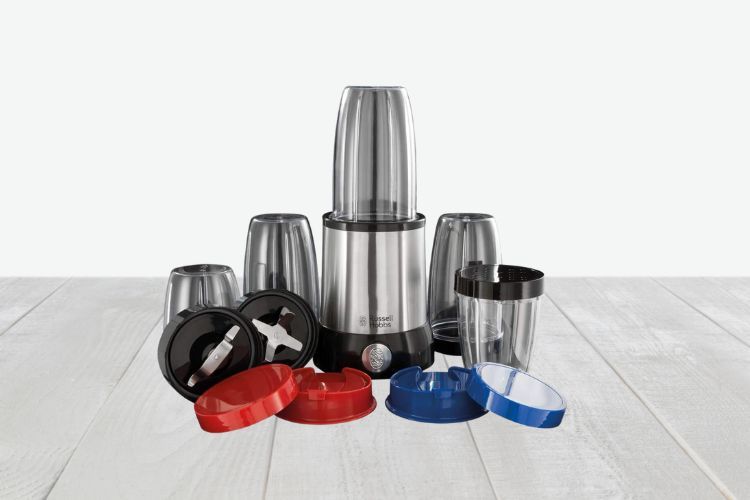 De Russell Hobbs Nutriboost Smoothie blenderset met een roestvrijstalen basis wordt omringd door verschillende accessoires, waaronder meerdere mengbekers van verschillende groottes, zwarte mesbevestigingen en kleurrijke deksels in rood, blauw en wit. Alle items worden tentoongesteld op een licht houten oppervlak.