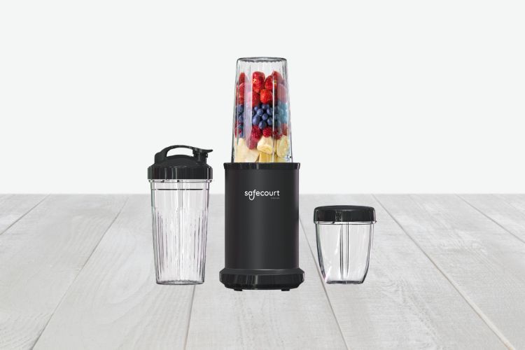 Een zwarte Safecourt Smoothie Blender staat op een licht houten oppervlak, de mengbeker is gevuld met een scala aan fruit. Naast de hoofdblender staan twee extra lege containers, één met deksel en één zonder, klaar voor uw volgende smoothiecreatie.