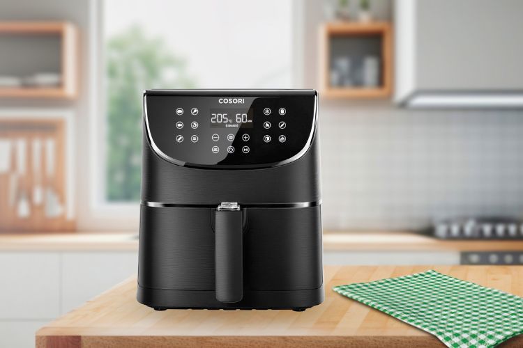 In een moderne keuken staat een zwarte Cosori XL Airfryer met een touchscreen op een houten aanrecht, naast een groen geruit tafelkleed.
