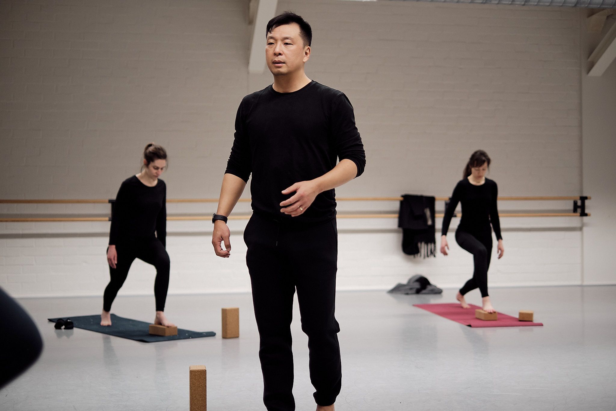 Justin Yep geeft yogales in de studio van Ndigo, twee deelnemers oefenen op matten op de achtergrond met yogablokken.