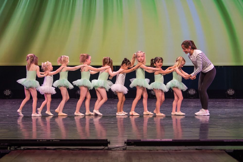 Kleuterdans bij Ndigo: jonge kinderen maken een rij op het podium in lichte balletkleding en de docent leidt hen.