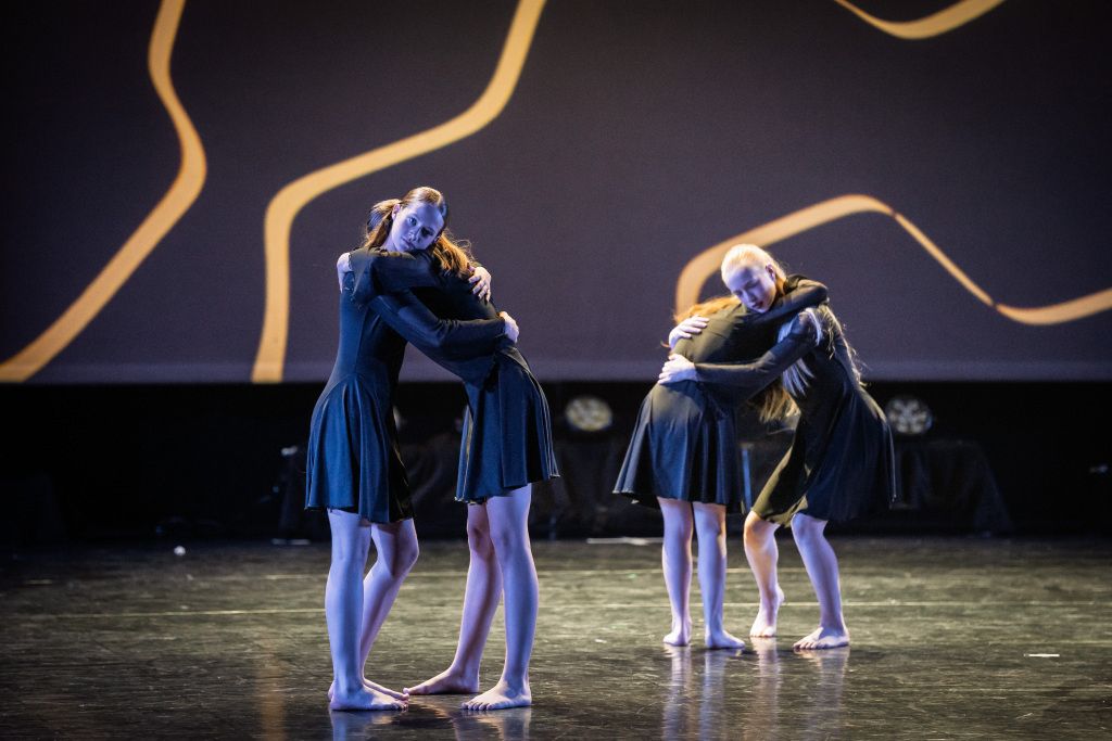 Tieners knuffelen elkaar op het podium tijdens moderne dans, als symbool voor steun, herstel en nieuwe focus na een slechte auditie.