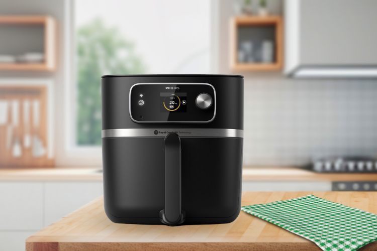 Op een houten aanrecht staat een zwarte Philips Airfryer Combi naast een groen geruit tafelkleed, met op de wazige achtergrond een moderne keuken.