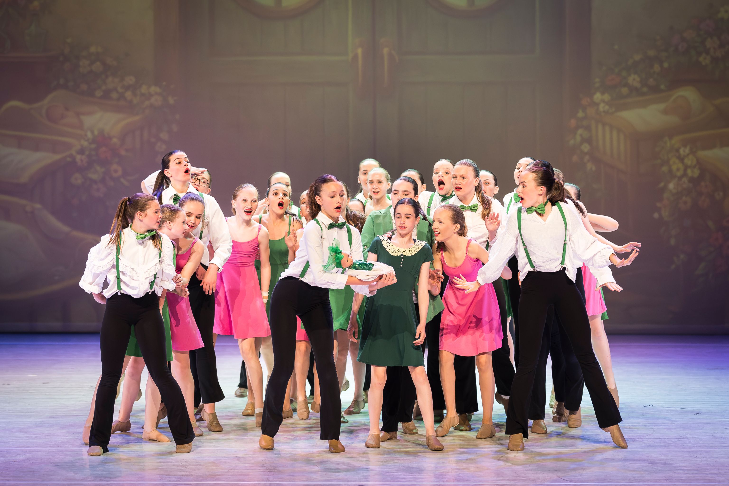 Groep jonge dansers van Ndigo op het podium tijdens een voorstelling, gekleed in kleurrijke kostuums van roze, groen en zwart-wit.
