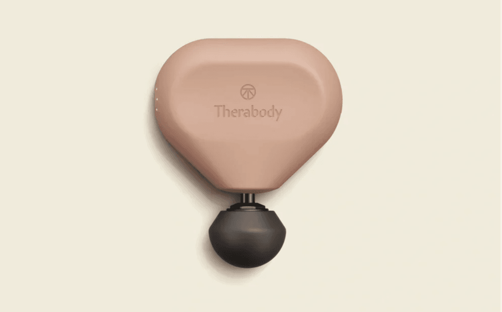 Een compact, zandkleurig Theragun Mini massagepistool met een ronde, draagbare vorm, een zwart bolopzetstuk en een discreet Therabody-logo op de bovenkant.
